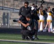 Photographer capturing sports event with telephoto lens on a sunny day at the stadium. Cheerleaders in the background.