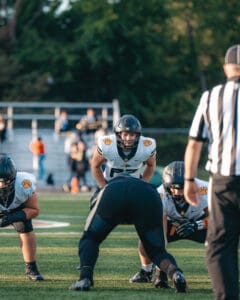 Football players in action during a game, with a referee observing on a sunny field.