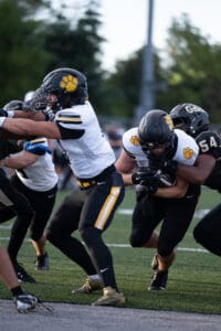 Football players in black and white uniforms tackle during a game on a green field.