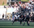 High school football game in action as players focus on strategy, surrounded by cheering crowd and cheerleaders.
