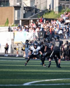 High school football game in action as players focus on strategy, surrounded by cheering crowd and cheerleaders.