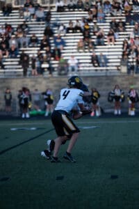 Football players in action on the field during a game, fans filling the stands in the background.