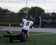 Football player tackled during a high school game on a field under a cloudy sky.