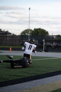 Football player tackled during a high school game on a field under a cloudy sky.