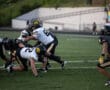 High school football players in action during a tackle on a green field, wearing black and white uniforms.