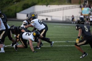 High school football players in action during a tackle on a green field, wearing black and white uniforms.