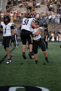 High school football players celebrate on the field during a game, showing teamwork and sportsmanship.