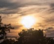 Sunset over silhouetted trees with dramatic clouds in the sky.