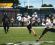 High school football quarterback runs with the ball during a game, evading a defender.