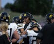 Football coach giving instructions to players on the sidelines during a game at dusk.