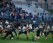 High school football game with teams in action on the field, surrounded by an audience in the stands.