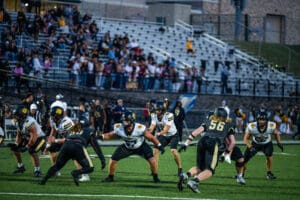 High school football game with teams in action on the field, surrounded by an audience in the stands.