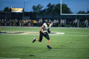 Football player runs on field during game, holding ball securely, with spectators in the background.