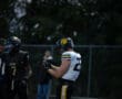 Football players on the field during a game, one wearing a black uniform, the other in white and yellow.