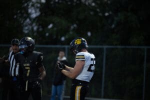 Football players on the field during a game, one wearing a black uniform, the other in white and yellow.