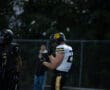 Football players during a game at night, one in white and yellow, another in black, with helmets and gear.