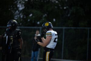 Football players during a game at night, one in white and yellow, another in black, with helmets and gear.