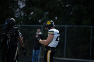Football players in action during a night game, wearing black and white uniforms with helmets.