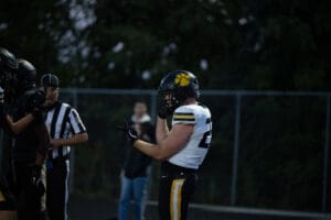 Football player in white and black uniform adjusts helmet during an evening game.