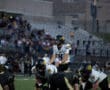 Football quarterback preparing for a play on the field during a night game with stadium crowd in the background.