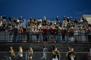 Crowd of enthusiastic fans in stadium bleachers during a nighttime sports event, enjoying the live action.