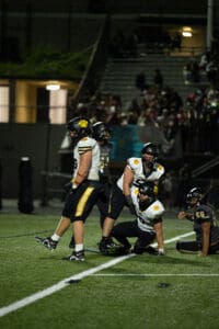 Football players during intense night game on field, audience in background.