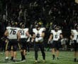 High school football team gathers on the field under stadium lights, preparing for a night game.