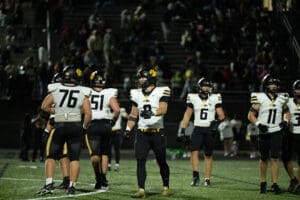 High school football team gathers on the field under stadium lights, preparing for a night game.