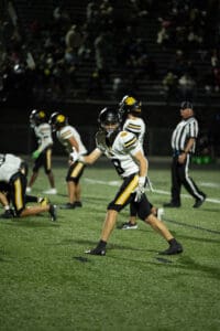 High school football player on field giving thumbs-up during night game.