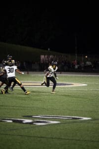 Football player in action during a night game, running with the ball on a lit field.