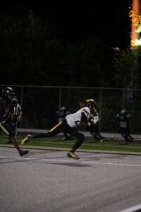 Football player making a dynamic run on the field at night during a game, wearing a black and yellow uniform.