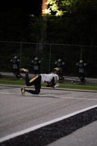 Football player makes a diving catch in the dark, wearing gold cleats and helmet on the field.