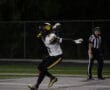 Football player celebrates on field under referee's watch during a night game.
