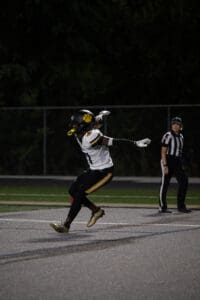 Football player celebrates on field under referee's watch during a night game.