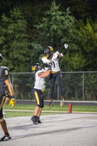 Football players celebrate a touchdown with a jump hug on the field at night.