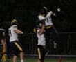 Football players celebrate a touchdown with a jump and lift under stadium lights during a night game.