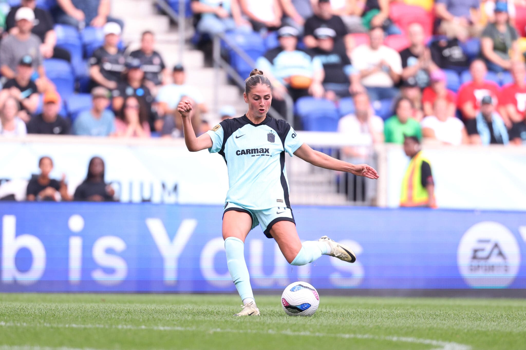 Soccer player in light blue kit kicking ball during match on sunny day at stadium.
