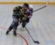 Two inline hockey players compete for the puck during an intense match on a rink.