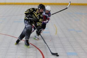 Two inline hockey players compete for the puck during an intense match on a rink.