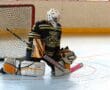 Roller hockey goalie in action, wearing protective gear, kneeling in front of net on rink.
