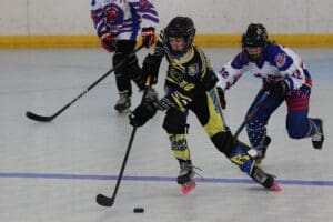 Youth roller hockey game in action with players competing for the puck on the rink.