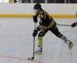 Inline hockey player in action on the rink, wearing yellow and black uniform, with a blue opponent in pursuit.