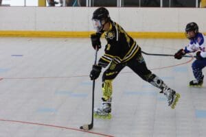 Inline hockey player in action on the rink, wearing yellow and black uniform, with a blue opponent in pursuit.