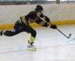 Inline hockey player in action, shooting the puck on goal while wearing a black and yellow uniform.