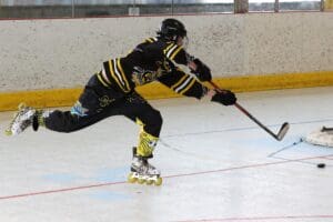 Inline hockey player in action, shooting the puck on goal while wearing a black and yellow uniform.