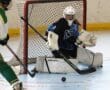 Roller hockey goalie defends against incoming puck, wearing blue jersey and white gear, focused on blocking the shot.