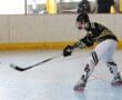 Roller hockey player in action on the rink, taking a shot with a black stick, wearing protective gear and skates.