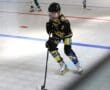 Youth inline hockey player in action on the rink, wearing black and yellow gear, focused on the game.