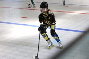 Youth inline hockey player in action on the rink, wearing black and yellow gear, focused on the game.