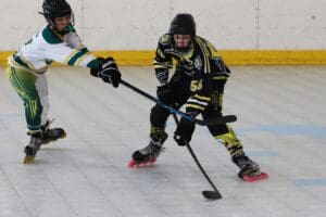 Two inline hockey players competing on an indoor rink, one making a defensive move.